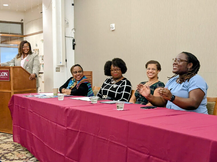 One woman at a podium and four women seated behind table in McBride Gathering Space